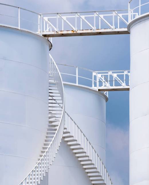 Low angle view of curve spiral staircase on white storage fuel tanks in vertical frame